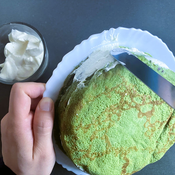spreading whipped cream on the sides of the matcha crepe cake