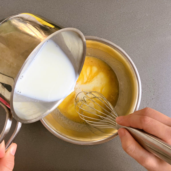 adding the heated milk to the custard